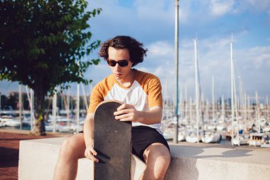 Şehre yakın oturan ve güneşli bir sokakta paten kaydıktan sonra dinlenen 20 'li yaşlarda, modaya uygun güneş gözlüklü, beyaz bir hippi hobiyle pratik yapmak için boş vakitleri düşünen genç bir kız.