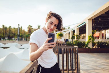 Neşeli nüfuz blogcusunun yarım boy portresi mobil uygulama vasıtasıyla medya içeriği yaratıyor ve kameraya gülümsüyor, cep telefonu teknolojisiyle cep telefonu teknolojisi ile kaygısız bin yıllık video çekiyor.