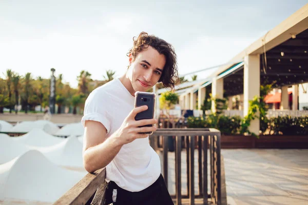 Neşeli nüfuz blogcusunun yarım boy portresi mobil uygulama vasıtasıyla medya içeriği yaratıyor ve kameraya gülümsüyor, cep telefonu teknolojisiyle cep telefonu teknolojisi ile kaygısız bin yıllık video çekiyor.