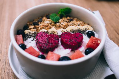 Lezzetli granola karpuzla süslenmiş ve nane şekerli yuvarlak kase ile süslenmiş. Restorandaki ahşap masada peçete var.