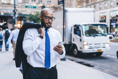 Kel sakallı, beyaz gömlekli, mavi kravatlı, omuzunda ceketi olan ve arka planda bulanık bir akıllı telefon kullanan Amerikalı patron.
