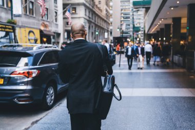 Katı takım elbiseli Afro-Amerikan bir çalışanın arka planda bulanık arka planda yol kenarında yürümesi.