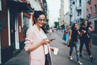 Keyifli hipster kızı şehir merkezinde boş zamanlarında ağ taramasından zevk alıyor, modern akıllı telefon aracılığıyla arkadaşlarıyla mesajlaşan mutlu İspanyol blogcu web rezervasyonları için 4G kablosuz internet kullanıyor