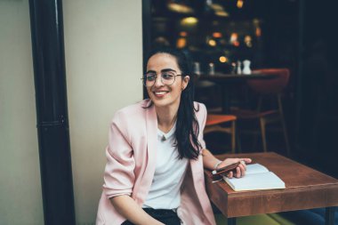 Klasik gözlüklü mutlu bayan öğrenci sokak kafeteryasında ders çalışıyor. Araştırma sırasında cep telefonu tutan güzel Gürcü kadın.