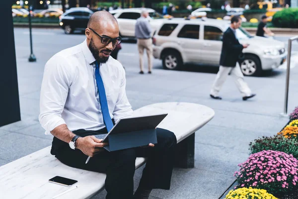 穿着衬衫和眼镜 头戴平板电脑 坐在长椅上 脚背模糊 街道拥挤的非洲裔美国男性员工感到欣慰 — 图库照片