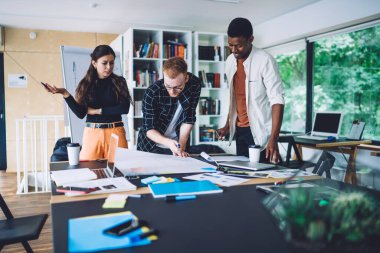 Mimari düzen için proje taslaklarıyla çalışan akıllı gelişigüzel gelişigüzel gelişmişlerden oluşan bir grup, fikir alışverişinde bulunan ve iletişim kuran masaüstü çizimleri üzerinde çalışan genç meslektaşlar.