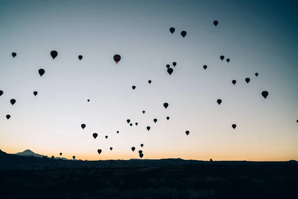 在黄昏时分 许多黑色气球的轮廓在高山上空飞舞 映衬着漆黑的落日的天空 — 图库照片