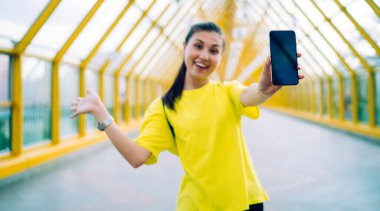 Aktif giyimli mutlu Asyalı hippi kız şehir ortamında boş zamanın ve mobil uygulamanın tadını çıkarıyor, bulanık arka planda neşeli kadın sosyal ağlarda web sayfası olan akıllı telefonu tutuyor.