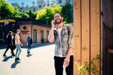 Neşeli erkek turistin yarım boy portresi akıllı telefon iletişimiyle solo turları tartışıyor klasik gözlüklü ve kot ceketli mutlu hippi cep telefonu uygulaması aracılığıyla gülümsüyor.