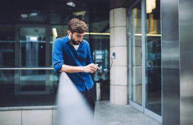 Gözlüklü ve gözlüklü, hayal kırıklığına uğramış genç sakallı erkek yaya geçidi köprüsünde beklerken buluşmayı bekliyor.