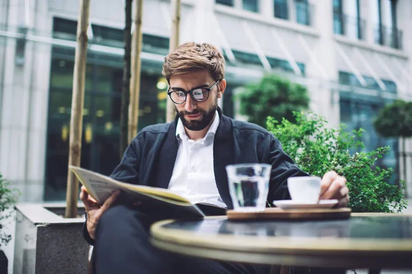 头戴眼镜 留着胡子 衣冠楚楚的商人 坐在餐桌旁 边喝咖啡边看报纸 边安静下来 — 图库照片