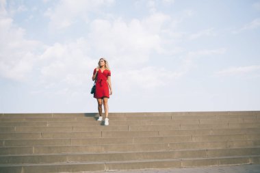 Modayı takip eden ufukta görünen şehir merdivenlerinde yürüyen şık kırmızı elbiseli beyaz turist, modaya uygun giyinmiş 20 'li yaşlarda tek başına gezen bayan gezgin.