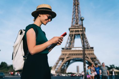Beyaz kadın Paris 'te romantik bir Fransız yürüyüşü için kablosuz ağda geziniyor, kaygısız bayan turist arka planda Eyfel Kulesi ile caddede duran akıllı telefon iletişiminin keyfini çıkarıyor.