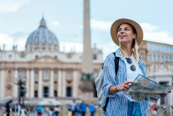 レクリエーション旅行中に気軽にバチカンの美しい建築を楽しむ藁帽子の女性観光客を笑顔 幸せなコーカサスのヒップスター女の子はローマの近くに観光ツアーを持っている地図を保持 — ストック写真