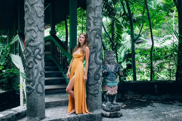 아름답고 여성으로 머리를 오렌지 드레스를 정글에서 조각품 전통적 보행자 다리의 — 스톡 사진