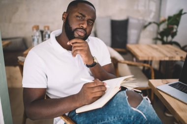 Ciddi koyu tenli erkek yazarın portresi. Telif defterindeki notlar üzerinde kafa yoruyor. Makale ve planlar yaratıyor.