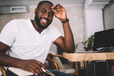 Kafede dizüstü bilgisayarla otururken kameraya bakıp el ele tutuşan gündelik kıyafetli mutlu Afro-Amerikan adam.