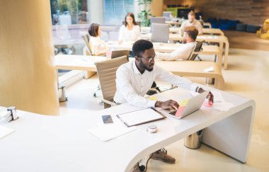 Proje için online araştırma yaparken çıkartma kullanan koyu tenli erkek profesyonel yöneticinin yukarıdan bakıldığında, laptopta bilgisayardan e-posta gönderen düşünceli adam çalışanı