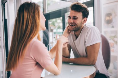 Romantik pozitif, birbirini seven çift kafe masasında komik bir sohbet sırasında birbirlerine dokunuyor ve nazikçe birbirlerine bakıyorlar.