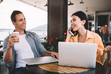 Neşeli iş arkadaşları birlikte parlak kafe terasında dizüstü bilgisayarları kullanarak kahvelerini yudumluyor kadın meslektaşlarıyla telefonda konuşurken mutlu mesut gülümsüyor birbirlerine neşeyle bakıyorlardı.