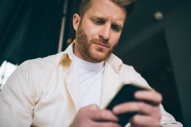 Şehirde oturan beyaz tişörtlü, konsantre sakallı bir adamdan iş hakkında mesaj almaya odaklanmış.