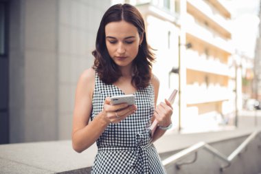 Not defteri ve saati olan ciddi bir kadın şehir merkezindeki korkulukların yanında duran akıllı telefonlu arkadaşına mesaj yolluyor. 