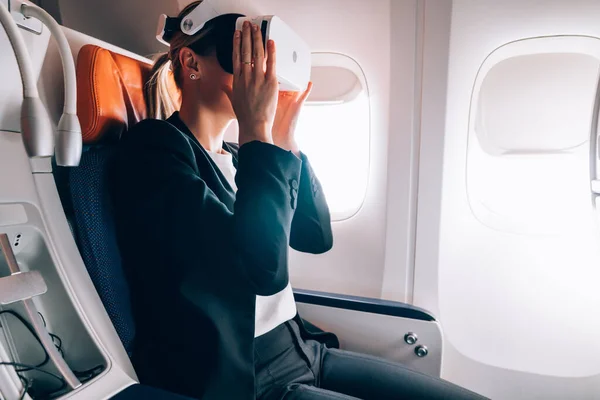Millennial woman watching 3d cinema video using modern applications from wearable VR glasses, formally dressed jetliner passenger in digital eyewear networking to stereoscopic augmented dimension
