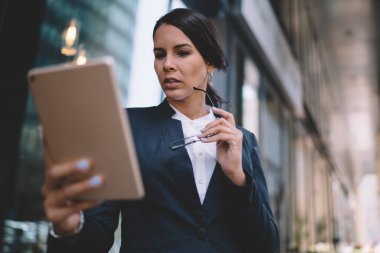 Resmi takım elbiseli karizmatik bayanın elinde gözlüklerle sokakta vakit geçiren tablet ekranına bakarken...