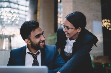 Mutlu etnik erkek ve kadın yönetici iş kıyafetleri giyip şehirde dizüstü bilgisayar kullanırken ve birbirlerine bakarken iş problemlerinin çözümünü bulmaya çalışıyorlar.
