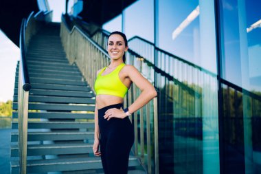 Aktif giyimli, sağlıklı yaşam tarzının keyfini çıkaran, hayat enerjisi ve esnekliğinin tadını çıkaran neşeli beyaz kadın portresi. Güzel, ince bir kız, fitness hedeflerine ulaşmak için kameraya bakıyor.