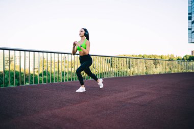  Aktif olarak çalışan genç, zayıf bir kadın stadyumda spor yapıyor, vücudunun alt kısımları için egzersiz yapıyor, Kafkasyalı bir kız forma hedeflerini koruyor, enerji için çalışıyor, kulaklıkla müzik dinliyor.