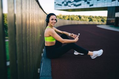  Aktif olarak çalışan genç, zayıf bir kadın stadyumda spor yapıyor, vücudunun alt kısımları için egzersiz yapıyor, Kafkasyalı bir kız forma hedeflerini koruyor, enerji için çalışıyor, kulaklıkla müzik dinliyor.