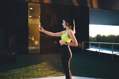  Aktif olarak çalışan genç, zayıf bir kadın stadyumda spor yapıyor, vücudunun alt kısımları için egzersiz yapıyor, Kafkasyalı bir kız forma hedeflerini koruyor, enerji için çalışıyor, kulaklıkla müzik dinliyor.