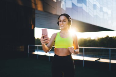  Aktif olarak çalışan genç, zayıf bir kadın stadyumda spor yapıyor, vücudunun alt kısımları için egzersiz yapıyor, Kafkasyalı bir kız forma hedeflerini koruyor, enerji için çalışıyor, kulaklıkla müzik dinliyor.