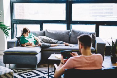 Milenyum çağındaki hipster bir adamın dijital tablette web sayfasına göz atması, koltukta oturup ilginç kitaplar okuması, birlikte vakit geçirmesi ve evde boş vakit geçirmesi.