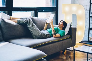 Gündelik giyinmiş güzel, ciddi bir yeniyetme kız rahat koltukta oturup kitap okuyor. Kafkasyalı 20 'li yaşlarda bir kadın oturma odasındaki kanepede uzanmış ilginç edebiyattan zevk alıyor.