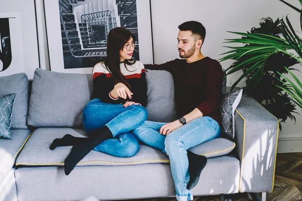 Positive male and female marriage sitting on sofa together communicating and resting on free time together, young marriage discussing relationships enjoying conversation in living room in apartment