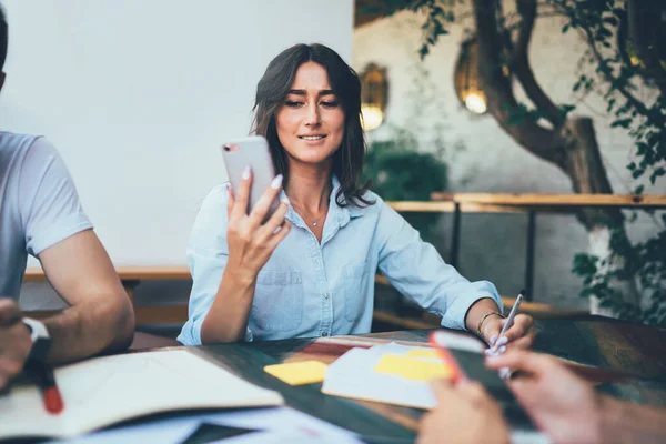 Attraktivt Leende Elegant Brunett Surfa Mobiltelefon Entusiastiskt Medan Skriver Anteckningsbok — Stockfoto