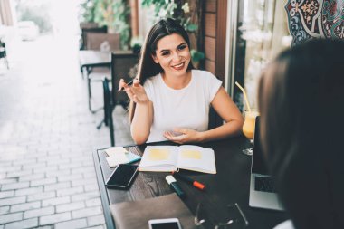 Dost canlısı, kalem ve açık defterli bir kadın, kaldırım kafesinde aletlerle masada otururken dizüstü bilgisayarlı potansiyel kadın adayla konuşuyor ve röportaj yapıyor.