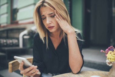 Modern cep telefonu kullanımından dolayı binlerce yıllık üzgün beyaz kadın baş ağrısı, dijital akıllı telefon teknolojisiyle ilgili e-posta mesajından hayal kırıklığına uğramış mutsuz hippi kız.