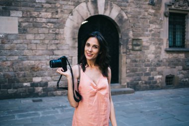 Üstü açılı, sıradan kıyafetleriyle gülümseyen, dijital kameralı muhteşem bir turist eski kasabadaki eski püskü taş binanın kemerli kapısında dikiliyor.