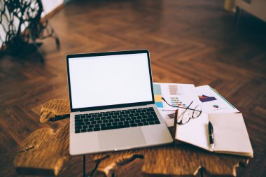 Yukarıdan renkli çizelgelerle boş ekranlı bir dizüstü bilgisayar ve modern apartmandaki ahşap kahve masasında gözlüklü bir dergi.