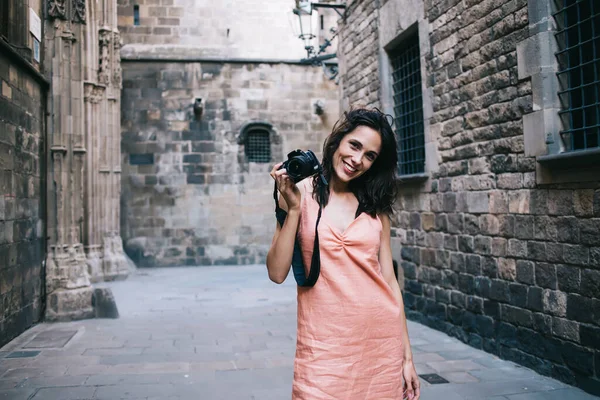 Ortaçağ şehrinde yaşlı binaların arasında durup kameraya gülümseyen ve fotoğraf makinesi tutan bir kadın.