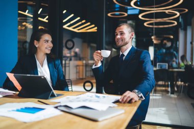 Başarılı bir adam ve kadın masaüstünde dijital teknolojiyle oturuyor ve kahve molası sırasında beyin fırtınası işbirliğinden ve girişimcilikten keyif alan neşeli profesyonellerden iletişim kuruyor.