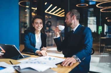 Başarılı bir adam ve kadın masaüstünde dijital teknolojiyle oturuyor ve kahve molası sırasında beyin fırtınası işbirliğinden ve girişimcilikten keyif alan neşeli profesyonellerden iletişim kuruyor.