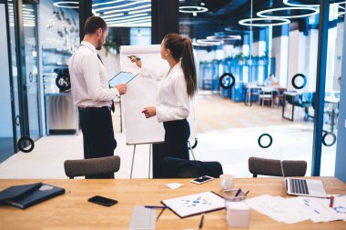 Profesyonel ekonomist, ortakla brifing sırasında proje bilgileri yazmak için beyaz tahtayı kullanıyor. Başarılı iş adamları birlikte çalışarak şirkette çözümler arıyor.