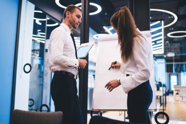 Profesyonel ekonomist, ortaklarla brifing sırasında proje için fikirler yazmak için beyaz tahtayı kullanıyor. Başarılı iş adamları birlikte çalışarak şirkette çözümler arıyorlar.