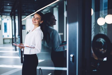 Resmi kıyafetler giymiş, elinde modern dijital tablet olan neşeli beyaz kadın, mesai saatlerinde kameraya gülümseyen, yarı boyda, neşeli bayan girişimci portresi.
