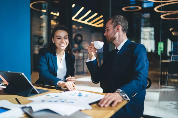 Başarılı bir adam ve kadın masaüstünde dijital teknolojiyle oturuyor ve kahve molası sırasında beyin fırtınası işbirliğinden ve girişimcilikten keyif alan neşeli profesyonellerden iletişim kuruyor.