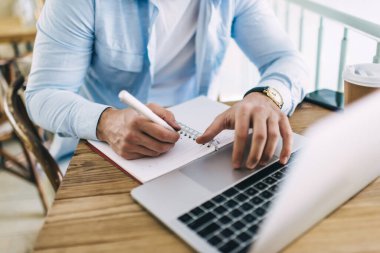 Not defterinde ödev yazan yetenekli bir erkek öğrencinin araştırma için dizüstü bilgisayar kullanması, teknolojiyi kullanarak kalem planlama projelerini elinde tutması ve kafedeki 4G bağlantısı.